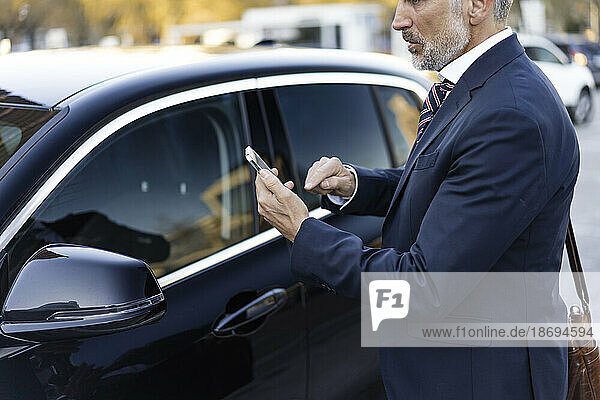 Businessman using smart phone standing near car