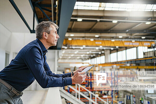 Businessman holding tablet PC leaning on railing in industry