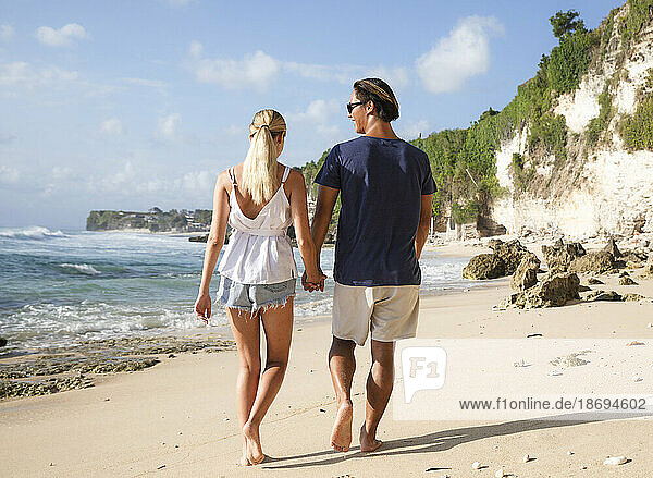 Glückliches junges Paar hält Händchen und geht am Strand spazieren
