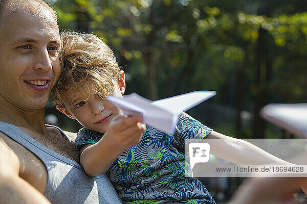Vater und Sohn spielen an einem sonnigen Tag mit einem Papierflieger