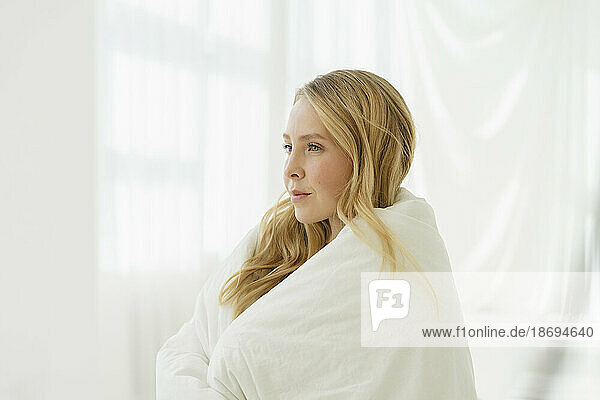 Woman wrapped in white blanket by translucent curtain