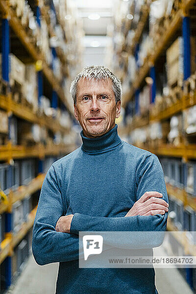 Confident mature businessman with arms crossed in warehouse