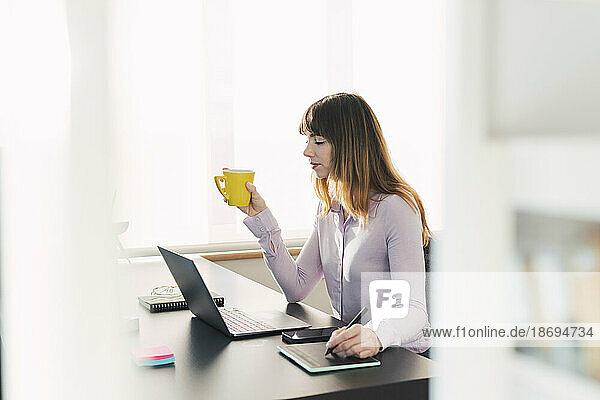 Geschäftsfrau mit Kaffeetasse sitzt am Schreibtisch
