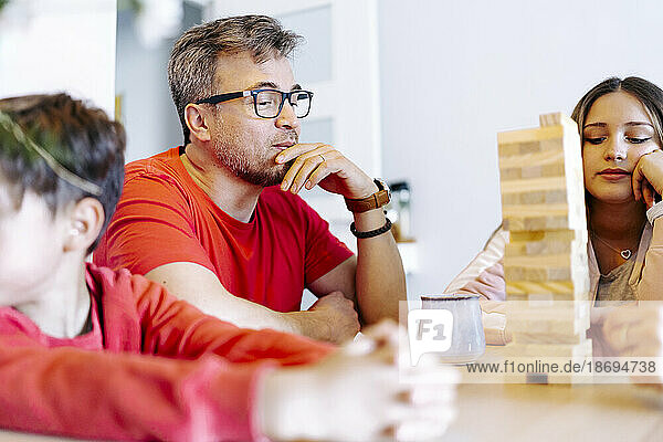 Thoughtful father playing block removal game with family at home