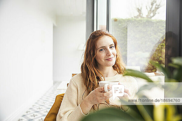 Smiling woman holding coffee cup by window