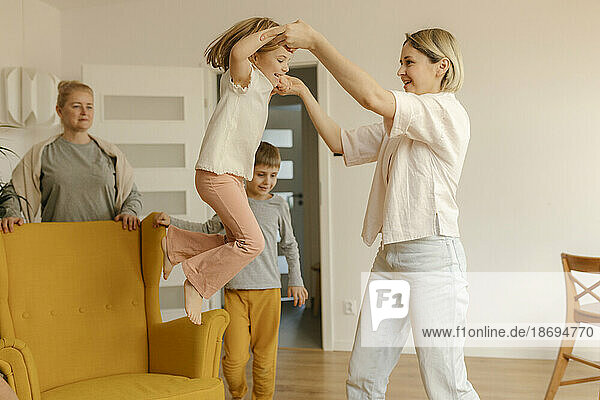 Mother assisting daughter jumping from armchair at home