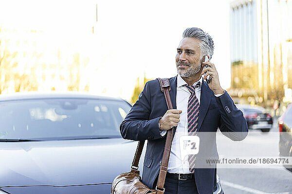 Businessman talking on smart phone standing near car