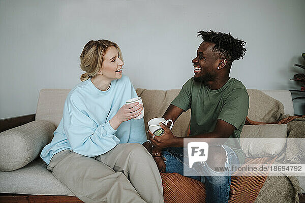 Happy couple enjoying coffee sitting on sofa at home