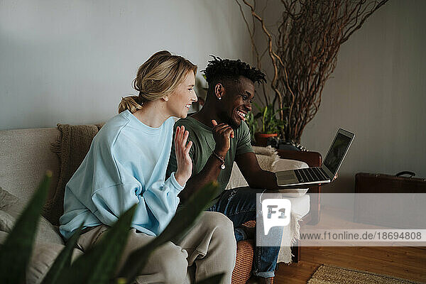 Happy couple gesturing on video call using laptop in living room at home