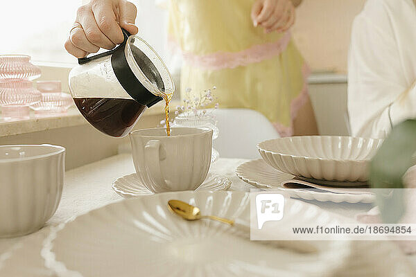 Frau gießt am Tisch zu Hause Kaffee in eine Tasse