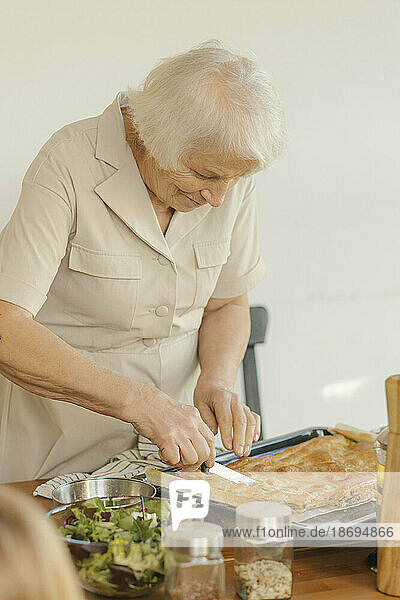 Elderly woman cutting cake at home