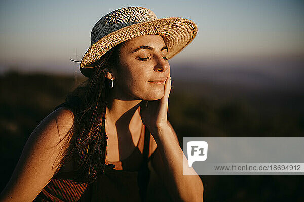Frau sitzt bei Sonnenuntergang mit der Hand am Kinn