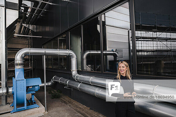 Lächelnde Geschäftsfrau steht neben Maschinenrohren in der Fabrik