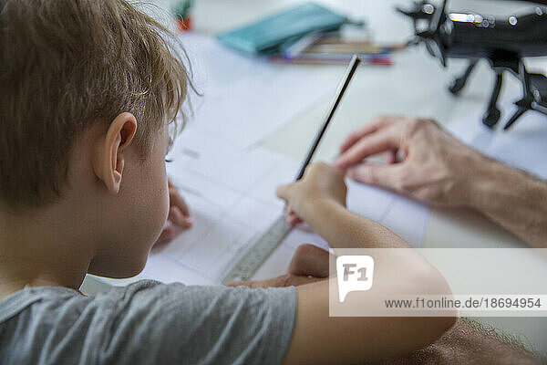 Father helping son drawing on paper at desk