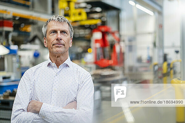 Thoughtful businessman with arms crossed at factory