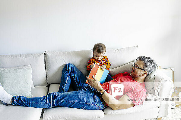 Father lying on sofa with son and book at home
