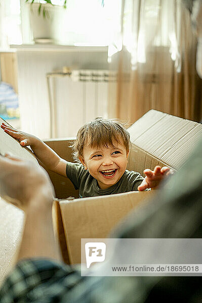 Fröhlicher Junge sitzt in einer Kiste und spielt zu Hause mit seinem Vater