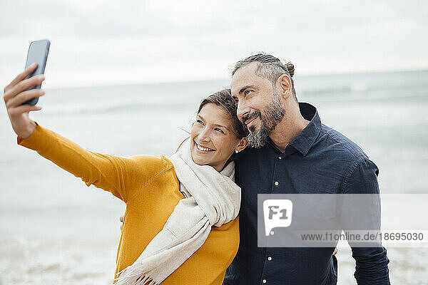 Happy couple taking selfie through smart phone at beach