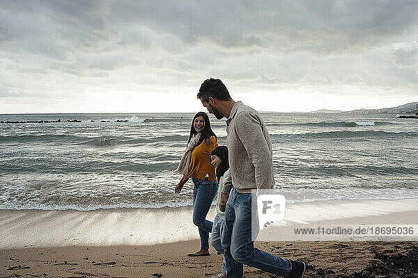 Glückliche Frau und Mann gehen mit Tochter am Strand spazieren