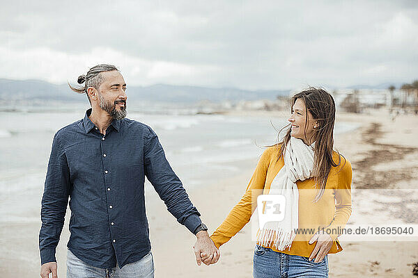 Smiling man and woman holding hands and walking at beach