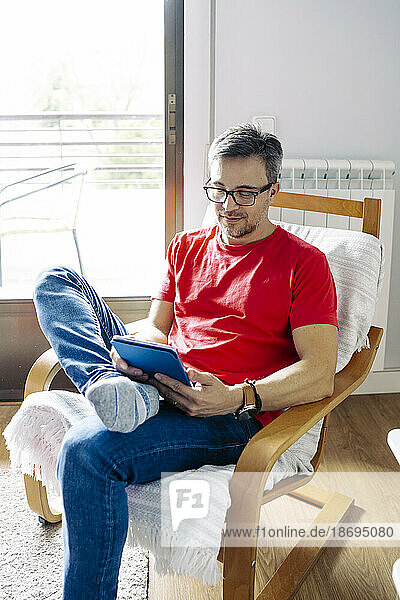 Man using tablet PC sitting on chair at home