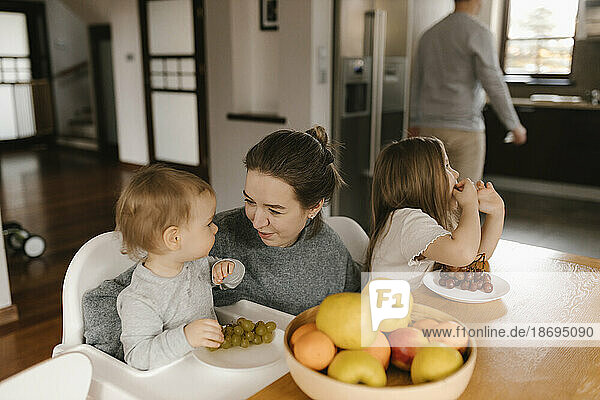 Mother with children eating fruit at dining table