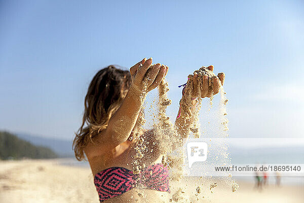 Junge Frau im Bikini gießt Sand am Strand