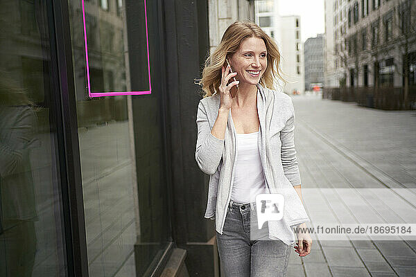 Smiling blond woman talking on smart phone at sidewalk