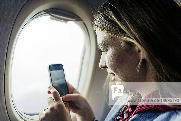 Frau fotografiert mit Smartphone im Flugzeug