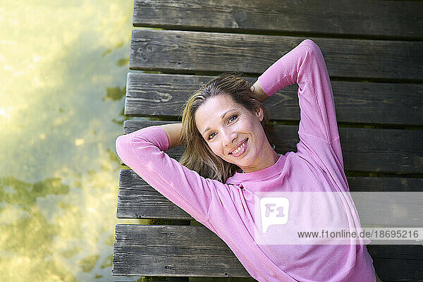 Smiling woman with hands behind head lying on boardwalk