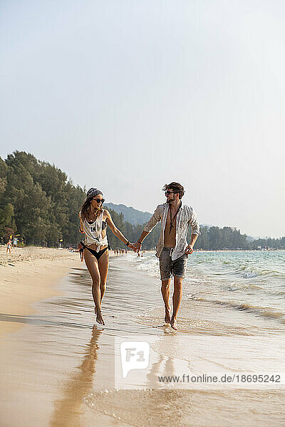 Couple holding hands walking near shore at beach
