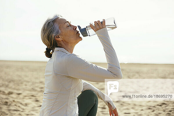 Frau sitzt am Strand und trinkt aus einer Wasserflasche