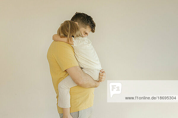 Father carrying daughter in front of wall