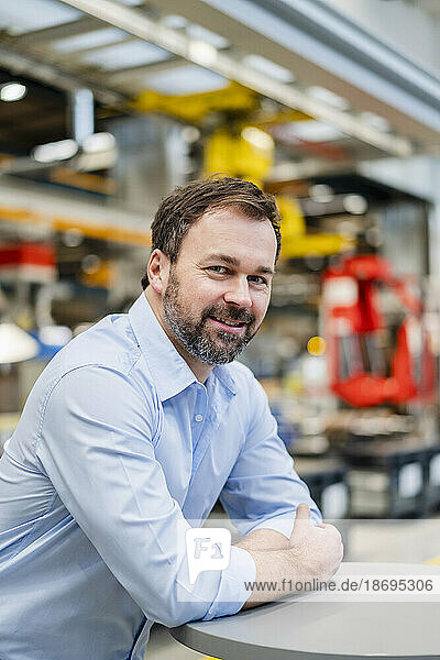 Smiling mature manager leaning on table in industry