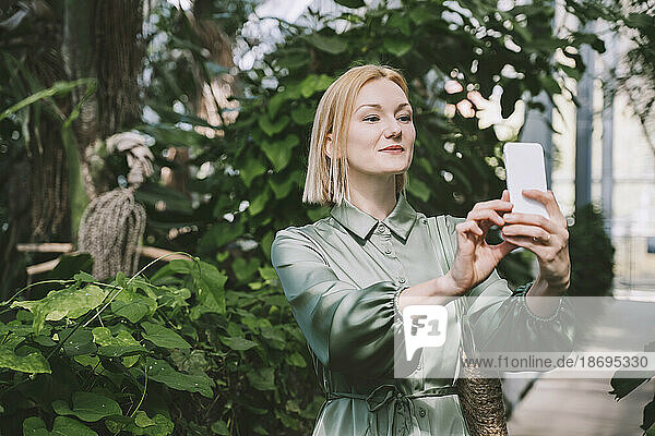 Woman taking selfie through smart phone in green house
