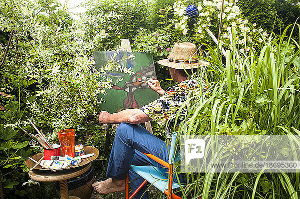 Man painting amidst plants sitting on chair in garden