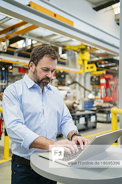Manager typing on laptop at table in factory