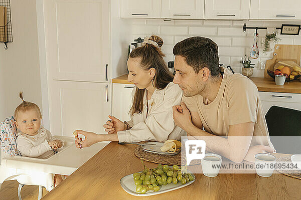 Father and mother with cute daughter eating fruit at home