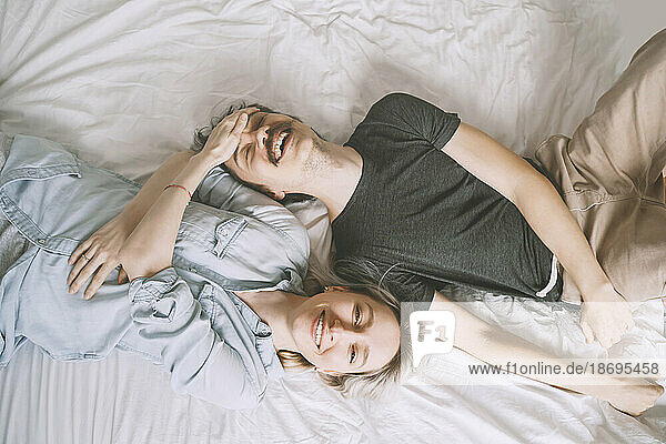 Smiling woman touching forehead of man lying on bed at home