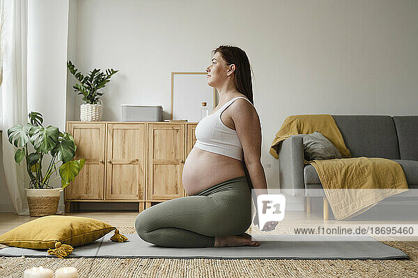 Pregnant woman stretching hands sitting on mat at home