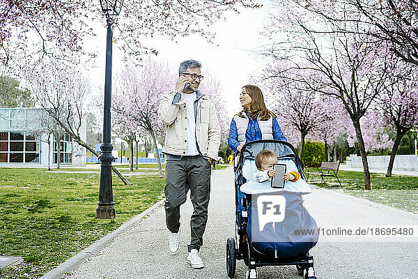 Father and mother walking with baby stroller on footpath at park