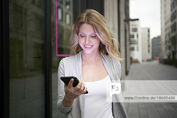 Smiling woman holding mobile phone at sidewalk
