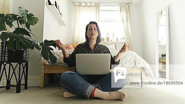 Woman meditating with laptop sitting cross-legged at home