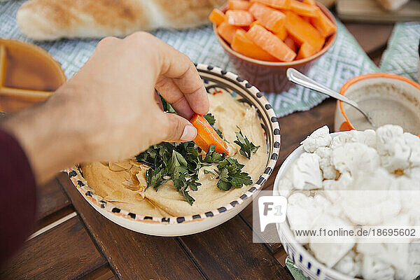 Hand nimmt Hummus mit Karotte am Tisch