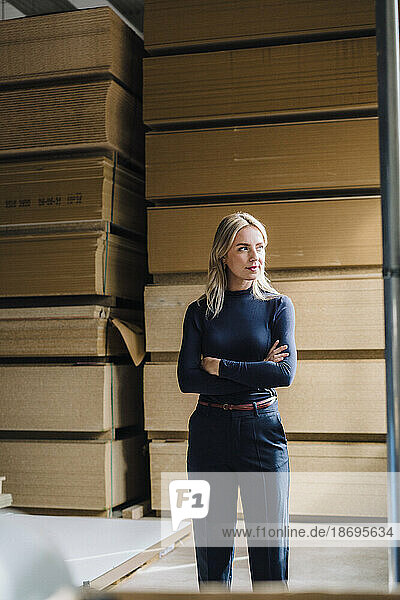 Thoughtful businesswoman with arms crossed in front of stacked wood