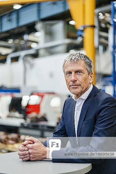 Confident businessman leaning on table at factory