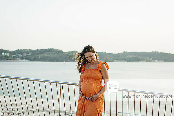 Smiling pregnant woman with hands on stomach by railing