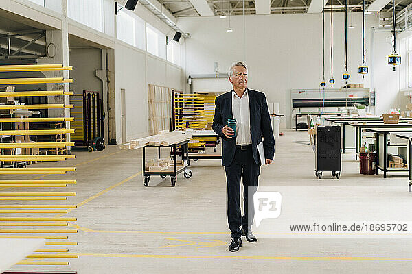 Businessman holding water bottle walking in factory