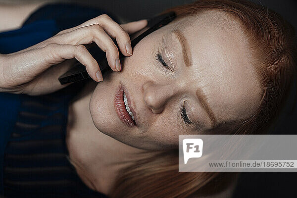 Young woman with eyes closed talking on smart phone