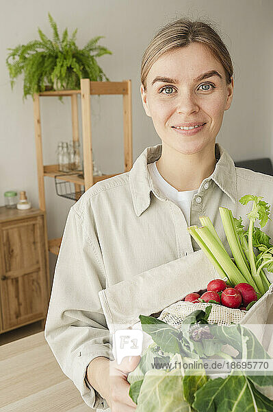 Smiling woman with bag of organic vegetables and fruits at home